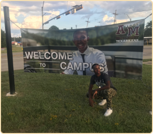 TAMUT Student Ambassador Lamonte Scott posing near campus entrance with billboard of himself. 